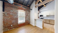 This one-bedroom, one-bathroom loft unit at 237-243 Furnace St in Akron, Ohio, masterfully blends historic industrial character with contemporary updates. The unit's most striking feature is its exposed red brick walls, which appear throughout the living area, bedroom, and kitchen, complemented by original timber beams and visible industrial ductwork that speak to the building's storied past. Soaring ceilings amplify the sense of openness across the compact yet efficiently laid-out floor plan. The living area features warm light hardwood flooring and benefits from natural light streaming through arched, multi-pane windows with wood trim — a signature architectural detail found throughout the unit. The kitchen is well-appointed with light wood cabinetry, a subway tile backsplash, stainless steel appliances including a range, microwave, and refrigerator, and a double sink — all set against a dramatic exposed brick backdrop. The spacious bedroom is carpeted for comfort, with the same soaring ceilings, exposed beams, and ductwork continuing the loft aesthetic. An in-unit washer is conveniently tucked into a dedicated closet near the entryway. The clean, modern bathroom features a tiled tub-shower combination, hardwood flooring, and a sleek vanity, offering a calm contrast to the unit's industrial elements.