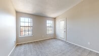 This single-floor residence offers a clean, functional layout with a neutral color palette throughout. The open living area features plush wall-to-wall carpeting and flows seamlessly into the kitchen, which is equipped with stainless steel appliances including a refrigerator, range, and over-the-range microwave. White cabinetry, light countertops, a tile backsplash, and warm hardwood-style flooring give the kitchen a bright, contemporary feel. A peninsula counter provides additional workspace and a natural transition to the living space.

The bedrooms are generously sized, each carpeted and filled with natural light from large gridded windows. Ceiling fans are present in the bedrooms, enhancing comfort year-round. The primary bedroom includes direct access to a walk-in closet and an en-suite bathroom, while an additional exterior-facing door in the living area allows for outdoor access and added light.

The bathroom features a white vanity with a single sink, light countertop, a large mirror, and a bathtub/shower combination, finished with hardwood-style flooring. Textured ceilings and clean white trim are consistent throughout, contributing to a cohesive and well-maintained interior aesthetic.
