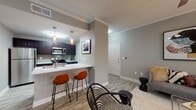 This apartment showcases a thoughtfully designed interior with a harmonious blend of style and functionality. The open-concept living area seamlessly connects the kitchen, dining, and living spaces. The kitchen boasts dark wood cabinetry, stainless steel appliances, and a convenient breakfast bar. The bedroom features a plush bed with a tufted headboard, ample natural light, and tasteful artwork. The bathroom offers a clean, modern aesthetic with a dark wood vanity and wood-look flooring. Throughout the space, neutral tones and contemporary furnishings create a cohesive, inviting ambiance. Additional amenities include in-unit laundry facilities and generous storage options.