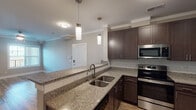 This single-floor residence offers a thoughtfully designed layout with a cohesive blend of modern finishes throughout. The kitchen serves as a centerpiece, showcasing rich dark-espresso cabinetry, speckled granite countertops, and a classic subway tile backsplash. Stainless steel appliances, including an electric range and built-in microwave, complement the space, while pendant lighting adds a refined touch above the granite-topped island with a double undermount sink. Wood-look luxury vinyl plank flooring flows through the main living areas and hallways, creating a warm, continuous aesthetic.

The living area features crown molding, a ceiling fan, and a window with natural light, opening through a hallway that connects to the rest of the unit. Two carpeted bedrooms each include ceiling fans and windows with exterior views, providing comfortable, well-lit spaces. The bathroom is finished consistently with the kitchen, featuring dark cabinetry, granite countertop, a framed mirror, and a full tub/shower combination set against light wood-look flooring. Neutral wall tones throughout the unit create a clean, move-in ready atmosphere.