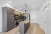 This contemporary apartment showcases a thoughtfully designed open-concept living space. The heart of the home is a modern kitchen, outfitted with sleek cabinetry in neutral tones, stainless steel appliances, and a practical island that doubles as a dining area. Pendant lighting adds a touch of style while illuminating the workspace.

The living areas are characterized by their spaciousness and abundance of natural light, courtesy of large windows that offer views of the surrounding area. Uniform light wood flooring runs throughout the apartment, creating a cohesive and warm atmosphere. The bedrooms are generously sized, with one featuring a walk-in closet for added convenience.

The bathroom is equipped with a bathtub-shower combination and appears to have clean, modern fixtures. Storage solutions are plentiful, with built-in closets and shelving units in various rooms. The apartment also includes in-unit laundry facilities, enhancing its practicality.

High ceilings and recessed lighting contribute to the overall sense of openness and modernity. The neutral color palette of whites and light grays provides a blank canvas for personal decorating styles. This well-designed space offers a perfect blend of comfort, functionality, and contemporary aesthetics.