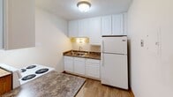 This single-floor residential unit offers a practical and comfortable layout designed for everyday living. The kitchen is well-appointed with crisp white cabinetry extending to the ceiling for ample storage, dark granite-style countertops, a double-basin sink, a white refrigerator, and an electric range. Wood-look flooring ties the kitchen together with a clean, modern feel.

The living area is generously sized, featuring neutral carpet, warm wood baseboards, a ceiling fan, and windows that bring in natural light and outdoor views. The open flow between the living and adjoining spaces provides a versatile environment suitable for various furniture arrangements.

The bedrooms are carpeted and offer comfortable proportions, each equipped with sliding wood-panel closets providing solid storage solutions. Ceiling fans are present, and windows allow for natural light and ventilation. Baseboard heating runs along the perimeter of the rooms, ensuring warmth throughout the unit.

The bathroom is clean and functional, featuring tile flooring, a granite-style vanity countertop with white cabinetry, a full tub and shower combination with white tile surround, and a grab bar for added convenience. Throughout the unit, textured ceilings, wood-toned doors, and consistent neutral tones create a cohesive and understated aesthetic.
