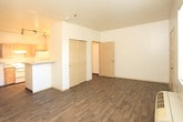 Located at 501 Coal Ave SW in Albuquerque, New Mexico, this single-story unit offers a practical and well-organized layout with consistent wood-look flooring running throughout every room. The living area is open and bright, featuring a window with blinds that allows natural light to fill the space, along with a wall-mounted HVAC unit for climate control. The room provides ample open floor space and connects smoothly to the rest of the unit. The galley-style kitchen is efficiently designed, lined on both sides with light wood cabinetry and speckled laminate countertops. It is equipped with a white electric range, a full-size refrigerator, a dishwasher, a microwave, and a single-basin sink, providing a complete set of appliances within a compact footprint. The bedroom is generously sized with warm-toned wood-look flooring, a double-door closet offering substantial storage, and access to adjacent rooms through paneled doors. The full bathroom features a vanity with a single sink and overhead cabinet, a standard toilet, and a tub-shower combination, all set on rich, dark wood-look flooring that adds warmth to the clean, neutral interior. Throughout the unit, the white walls and understated finishes create a clean, functional living environment.