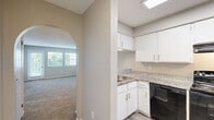 Located at 8619 E 61st Terr in Kansas City, MO, this two-bedroom, one-bathroom unit offers a functional single-floor layout designed for comfortable everyday living. The combined kitchen and living area forms the heart of the home, featuring a peninsula with granite-look countertops that separates the two spaces. The kitchen is well-equipped with white cabinetry, light wood-look flooring, and black appliances including a refrigerator, electric range with overhead hood, and dishwasher. A charming arched passageway connects the kitchen area to the hallway, adding a subtle architectural detail. The spacious living room is carpeted and benefits from multiple windows and a glass door that invite natural light and outdoor views. Both bedrooms are carpeted and feature neutral gray walls with textured ceilings. The primary bedroom includes a sliding closet and access to the hallway. The second bedroom is bright, with corner windows offering outdoor views. The full bathroom is finished with white subway-style tile surrounding a tub-shower combination with chrome fixtures and wood-look flooring. Throughout the unit, a consistent neutral color palette and practical finishes create a clean, cohesive living environment.