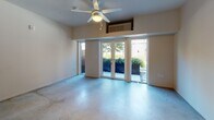 This single-floor unit offers a thoughtfully designed layout with a modern aesthetic throughout. The living area is a highlight of the space, featuring polished concrete floors that extend throughout most of the unit, a ceiling fan with overhead lighting, and a wall-mounted HVAC unit. Large glass French doors flood the room with natural light and provide direct access to an outdoor patio area, where greenery is visible beyond, creating a pleasant indoor-outdoor connection.

The kitchen is efficiently laid out and features sleek white cabinetry, grey countertops, and a striking dark tile backsplash that adds contrast to the clean palette. Open wood-framed shelving adds warmth above the counters, and the space is equipped with a white electric range, an over-the-range microwave, a refrigerator, and a single-basin stainless steel sink.

The bedroom is a well-proportioned room distinguished by bold matte black sliding closet doors, which provide a striking visual contrast against the neutral walls and concrete flooring.

The bathroom maintains the unit's clean, contemporary style with white cabinetry, a grey countertop vanity with an undermount sink, a large mirror, and a full tub-shower combination. A vibrant teal floor adds a distinctive pop of color to the otherwise crisp white space.