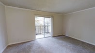 This single-floor residence offers a clean, functional layout designed for comfortable everyday living. The living area serves as the heart of the space, characterized by soft wall-to-wall carpeting that adds warmth underfoot and a textured ceiling that lends a classic residential feel. Crown molding runs along the perimeter of the room, providing a refined architectural detail that frames the space with understated elegance.

A prominent sliding glass door fills the room with an abundance of natural light, creating a bright and airy atmosphere throughout the day. The door opens directly onto a private balcony enclosed by a wooden railing, offering a pleasant outdoor retreat with views of surrounding trees and neighboring structures — ideal for enjoying fresh air in a semi-private setting.

The neutral, light-toned walls provide a versatile backdrop that complements a wide range of interior styles and furnishing choices. The overall ambiance of the space is calm and welcoming, with a straightforward, practical design that prioritizes livability. The single-floor layout ensures easy accessibility and a seamless flow throughout the unit, making it a well-suited option for those seeking a low-maintenance yet comfortable living environment.
