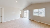 Unit 1576-03 is a modern two-story townhome offering 1,750 square feet of thoughtfully designed living space across three bedrooms, two bathrooms, a loft, and an attached garage. The main living level spans 1,480 square feet and centers around an open-concept kitchen and living room with vaulted ceilings and light hardwood-style flooring. The kitchen is equipped with stainless steel appliances, including a French door refrigerator, electric range, and built-in microwave, complemented by warm wood cabinetry and light quartz countertops. Sliding glass doors lead from the living area to a private balcony overlooking the community. The bedrooms feature plush carpeting and large windows that bring in natural light. The primary bedroom measures a generous 330 square feet and is served by a well-appointed bathroom with a double-sink vanity, rich wood cabinetry, and modern light fixtures. A dedicated laundry room houses a full-size Whirlpool washer and dryer with overhead cabinetry for added storage. Two closets and a hallway provide additional organization. The ground floor includes a 270-square-foot attached garage with concrete flooring. A loft and two staircases round out this functional, contemporary home within a newly developed community.