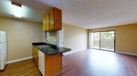 Located at 601-645 Sea Vale St in Chula Vista, California, this single-story unit offers a functional and comfortable layout with a cohesive design throughout. The kitchen is well-appointed with warm oak cabinetry lining both sides of the galley-style space, striking dark granite countertops, a double sink, white appliances including a range and refrigerator, and a built-in microwave. A peninsula counter extends toward the living area, creating a natural transition between the two spaces. The open living area features rich hardwood-style flooring and is bathed in natural light from a large sliding glass door that opens to an outdoor patio, offering pleasant views of surrounding greenery. A ceiling fan adds to the comfort of the space. The bedroom is generously sized with plush carpeting, a wide window that frames outdoor views, and a wall-mounted thermostat for individual climate control. The bathroom is finished with the same dark granite countertop as the kitchen, an undermount sink with brushed nickel fixtures, a large wall mirror, and a separate shower area. Warm beige tones carry throughout the unit, and textured ceilings are present in each room, contributing to the overall character of this well-maintained Chula Vista residence.