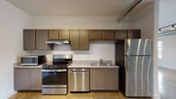 Located in Memphis, TN 38104, this single-floor studio unit blends industrial aesthetics with modern conveniences in an open, airy layout. Polished concrete floors run throughout the entire space, lending a sleek, urban character that ties each area together seamlessly.

The open-concept main living area is filled with natural light from multiple windows fitted with blinds, offering views of the surrounding neighborhood. Exposed spiral ductwork runs along the ceiling, complementing the industrial design, while adjustable track lighting provides targeted illumination. A ceiling fan adds to the comfort of the space.

The kitchen is well-appointed with warm-toned shaker-style cabinetry, granite-look countertops, and a full suite of stainless steel appliances including a gas range, dishwasher, refrigerator, and microwave. An under-cabinet range hood and double-basin sink complete the functional kitchen setup. In-unit laundry is also available.

The bathroom features a clean, minimalist design with a bathtub/shower combination and continues the polished concrete flooring found throughout the unit. Crisp white walls keep the space feeling bright and fresh.

With its bold navy accent wall in the living area, exposed mechanical elements, and durable finishes, this unit offers a distinctive industrial-modern character ideally suited for urban living in Memphis.
