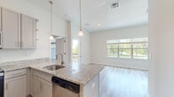 This thoughtfully designed one-bedroom, one-bathroom unit spans two floors, offering a functional and modern living experience. The main living floor features light-toned hardwood-style flooring throughout the open-concept living and kitchen areas. A large picture window in the living area floods the space with natural light and provides views of surrounding greenery, creating a bright and welcoming atmosphere.

The kitchen is a standout feature, equipped with granite countertops, gray shaker-style cabinetry, stainless steel appliances including a refrigerator, range, microwave, and dishwasher, and a peninsula with pendant lighting overhead. A door from the kitchen provides access to a private balcony.

A hallway leads to the generously sized bedroom, which features plush carpeting, elevated ceilings, a walk-in closet, and a window with outdoor views. The full bathroom is finished with dual undermount sinks set in granite countertops, gray cabinetry, a large mirror, and a tub-shower combination. Consistent neutral tones and quality finishes throughout give the unit a clean, contemporary aesthetic.