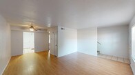 This two-story townhome provides a practical and comfortable layout across two levels. The main floor features an open living area finished with warm wood-style laminate flooring, neutral white walls, and a ceiling fan, creating a bright and airy atmosphere. A staircase connects the main level to the upper floor, and tile flooring transitions into the entry and kitchen areas. The kitchen is designed in a galley style, featuring white cabinetry, ample counter space, a double basin sink, and white appliances including a range and refrigerator, with tile flooring throughout.

Upstairs, the bedrooms are carpeted for comfort and each includes a ceiling fan with light fixture. The primary bedroom features direct access to an en-suite bathroom and a walk-in closet, providing added convenience and storage. Additional bedrooms are well-proportioned with natural light from windows. The bathrooms are finished with tile flooring, white vanity cabinetry, and large mirrors. Built-in linen storage is present in the bathrooms, adding functional storage throughout the home. Overall, the townhome presents a clean, neutral palette well-suited for a variety of living arrangements.
