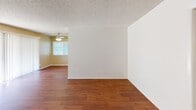 Located at 1950-2010 E Santa Clara Ave in Santa Ana, California, this single-floor residence offers a practical and comfortable layout throughout. The living area features rich hardwood-style flooring and a ceiling fan, creating a warm and inviting atmosphere. Natural light filters in through horizontal blinds, enhancing the open feel of the space. The kitchen is efficiently designed with white cabinetry, laminate countertops, a coil-burner electric range, and hardwood-style flooring that continues from the living area. A recessed ceiling detail adds a subtle architectural accent overhead. The bedroom is generously sized with soft wall-to-wall carpeting, a ceiling fan, and a window that brings in natural light. A standout feature of the bedroom is the expansive mirrored sliding closet doors, which provide ample storage with built-in shelving while visually expanding the room. The bathroom includes a large vanity with a single sink, framed mirror, and warm hardwood-style flooring. A separate water closet offers added privacy. Throughout the residence, textured ceilings, clean white walls, and consistent finishes contribute to a cohesive and well-maintained interior character.
