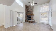 This two-story home makes an immediate impression with its soaring vaulted living room, where a striking floor-to-ceiling river rock fireplace serves as the undeniable focal point. The fireplace, constructed from rounded natural stones and topped with a solid wood mantel, rises dramatically toward the high ceiling, complemented by light wood flooring, abundant natural light from large windows, and a sliding glass door that opens to an outdoor balcony or patio area. A ceiling fan overhead adds both function and style to this expansive main living space.

The kitchen is designed for practicality, featuring light wood cabinetry, white countertops, and stainless steel appliances including a range, microwave, and refrigerator. Light wood-look flooring continues through this space, and a window brings in natural light. The layout offers generous counter and storage space throughout.

The bedrooms are comfortably sized, each featuring plush neutral carpeting, ceiling fans, and sliding glass doors or windows that connect to the outdoors. The primary bathroom is equipped with a dual-sink vanity, wood-toned cabinetry, and a large mirror. Additional bathrooms throughout the home maintain a clean, neutral aesthetic with wood-toned vanities and light flooring, ensuring comfort across both floors.