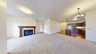 This single-floor residence offers a well-considered layout that balances comfort and functionality throughout its living spaces. The expansive living room serves as the heart of the home, anchored by a wood-mantled fireplace with a tile surround, adding warmth and character to the space. Plush wall-to-wall carpeting extends across the living area, while a glass-paneled exterior door provides access and brings in natural light. Crown molding adds a refined architectural detail to the main living space.

The kitchen is thoughtfully designed with rich, dark wood cabinetry, granite countertops, and stainless steel appliances including a full-size refrigerator and range. A center island with additional counter space and storage provides a practical workspace, while pendant lighting overhead and hardwood flooring complete the area.

A bedroom features sliding glass doors that open to a private balcony with views of the surrounding building exterior, adding an outdoor connection. The bathroom is equipped with accessibility-friendly grab bars and tile flooring. A dedicated laundry room includes a full-size washer and dryer alongside upper cabinetry for storage, set on durable tile flooring. The overall palette of warm whites and neutral tones creates a cohesive, inviting atmosphere throughout.