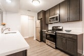 Located at 200 Springfield Ave in Springfield, NJ, this single-floor residence offers a clean, modern aesthetic with quality finishes across every room. The open-concept living and dining area is anchored by warm wood-look luxury vinyl flooring, crown molding, and a chandelier that adds an elegant touch. A pass-through opening connects the living space seamlessly to the kitchen, which features rich dark cabinetry, white quartz countertops, a classic subway tile backsplash, and stainless steel appliances including a gas range, microwave, and refrigerator — all complemented by a double-basin sink along the peninsula. The bedrooms are carpeted for comfort and filled with natural light through large windows that offer views of the surrounding greenery, with one bedroom featuring a corner window configuration. The primary bathroom showcases striking marble-style tile on both the floors and walk-in shower surround, enclosed by sleek frameless glass sliding doors and finished with brushed nickel hardware. A second full bathroom features large-format gray tile flooring, dark vanity cabinetry, white countertops, and a combined tub and shower with a window for natural light. Throughout, the space maintains a bright, neutral palette that creates a welcoming and move-in-ready atmosphere.