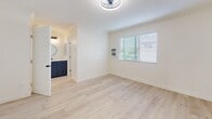 Located in Newport Beach, California, this thoughtfully updated one-bedroom, one-bathroom unit offers a clean, modern aesthetic throughout. Light wood-style flooring runs continuously across the entire space, complementing the crisp white walls and creating a bright, airy atmosphere.

The open-concept kitchen features a peninsula with a white quartz-style countertop, white shaker cabinetry extending to the ceiling for generous storage, and stainless steel appliances including a refrigerator and microwave. Sleek black pendant lights hang above the peninsula, adding a contemporary contrast to the otherwise light palette.

The spacious primary bedroom is generously sized, fitted with a modern ceiling fan and light fixture, crown molding, and a large window dressed with horizontal blinds that invite natural light while maintaining privacy. A dedicated closet and direct access to the bathroom provide added functionality.

The bathroom is well-appointed with navy blue cabinetry topped with a light countertop and a round mirror, paired with a combined shower and tub enclosed by a sliding glass door with matte black hardware and marble-style tile surround. Recessed lighting throughout the living areas and bedroom ensures consistent, clean illumination across the entire unit.

Situated at Superior Ave in Newport Beach, this unit offers proximity to the beach, dining, and all coastal amenities.