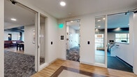 Located at 1160 Frost Ave in Maplewood, Minnesota, this expansive amenity floor offers a thoughtfully designed collection of communal spaces spanning a generously sized single level. The layout is connected by a clean, modern hallway finished with light hardwood flooring, herringbone-patterned inlays, and keycard-secured access points that lead residents to each area.

The lounge spaces are a standout highlight, featuring bold teal accent walls with decorative paneling, warm caramel leather sofas, and a contemporary gold chandelier. Large floor-to-ceiling windows flood the seating areas with abundant natural light and frame views of the surrounding greenery. A wall-mounted television and sleek coffee table complete the gathering space, making it ideal for both relaxation and socializing.

An additional common area showcases a striking decorative ceiling, patterned carpeting, and a mix of casual seating arrangements alongside a kitchenette equipped with cabinetry and appliances, providing a functional space for community events.

The fitness center is well-appointed with multiple treadmills, free weights, kettlebells, and cardio equipment, all set against floor-to-ceiling mirrors and dark teal accent beams. Ceiling fans and large windows overlooking the exterior keep the space bright and well-ventilated. The overall design palette—neutral walls, warm wood floors, and deep teal accents—creates a cohesive, modern aesthetic throughout.