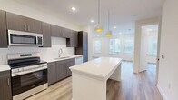 This well-designed one-bedroom, one-bathroom unit offers a thoughtful layout across a single floor, making efficient use of its space. The open-concept kitchen and living area serves as the heart of the home, featuring dark espresso cabinetry that contrasts beautifully with the bright white quartz island and countertops. A full suite of stainless steel appliances — including a French door refrigerator, range, microwave, and dishwasher — provides modern functionality. Stylish globe pendant lights with gold interiors hang above the island, adding a warm contemporary touch. Light wood-style flooring runs throughout, unifying the space with a clean, cohesive aesthetic. Large windows fitted with horizontal blinds invite abundant natural light into both the living area and the bedroom, creating an airy and welcoming ambiance. The bedroom is comfortably sized, equipped with a ceiling fan and multiple windows. Two closets provide generous storage, including a walk-in closet with built-in shelving and hanging rods. The bathroom features a glass-enclosed marble-tiled shower and continues the home's modern design language. An in-unit laundry area adds everyday convenience. Recessed lighting throughout completes the polished, move-in-ready feel of this contemporary residence.