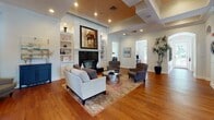 This single-story home showcases a refined interior defined by warm hardwood flooring, crown molding, and an elegant neutral palette that flows consistently throughout. The expansive living room serves as the heart of the home, anchored by a striking floor-to-ceiling fireplace with a dark surround, flanked by built-in shelving with cabinet storage below. A tray ceiling with recessed lighting adds architectural depth and visual interest to this generously proportioned space.

The home features two distinct dining areas. A formal dining room accommodates a large dark wood table with seating for eight, benefiting from abundant natural light through multi-pane windows and a glass-paneled exterior door with outdoor views. A secondary dining space features a round glass-top table beneath a statement pendant light, with tall windows dressed in flowing drapes and decorative accents completing the room.

The kitchen is outfitted with crisp white cabinetry, dark granite countertops, and stainless steel appliances, offering a clean, functional workspace with natural light from a nearby window. Crown molding, chair rail detailing, and consistent hardwood flooring unify the home's overall aesthetic, creating a cohesive and welcoming living environment.