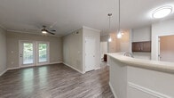 Located in Columbus, Georgia, this single-story, 2-bedroom, 2-bathroom home offers a well-designed layout with a comfortable flow throughout. The open-concept living, dining, and kitchen area serves as the heart of the home, featuring wood-look vinyl plank flooring, crown molding, and elegant pendant lighting above the dining space. The kitchen is equipped with rich dark-wood cabinetry, light countertops, a tile backsplash, and black appliances, including a refrigerator, range, and microwave. A breakfast bar connects the kitchen to the dining area for easy entertaining. Both bedrooms are carpeted and generously sized, with the primary bedroom offering a ceiling fan and a large window that invites natural light and views of surrounding greenery. Each bedroom is paired with a closet featuring wire shelving systems for organized storage. The bathrooms are finished with wood-look flooring, dark vanity cabinetry, and a tiled tub-shower combination with brushed nickel fixtures. A dedicated laundry room with washer and dryer connections adds everyday convenience. A covered outdoor porch with wood-beam ceiling detailing provides a pleasant space to relax. Neutral tones throughout create a cohesive and inviting atmosphere.