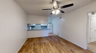 This efficient single-floor residence offers a thoughtfully arranged layout across one bedroom and one bathroom. The combined kitchen and living area serves as the heart of the home, where warm wood-look flooring transitions seamlessly into terracotta tile near the entryway. The kitchen features white cabinetry, a stone-tile backsplash, gray countertops with a breakfast bar peninsula, and white appliances including a range, dishwasher, and refrigerator. A ceiling fan with integrated lighting overhead keeps the open living space comfortable and well-lit. The spacious bedroom is carpeted for warmth and comfort, featuring a ceiling fan, a window that allows natural light to filter in, and access to a generous closet with a full-width hanging rod. The bathroom includes a wide vanity with gray countertops, ample cabinet storage, a large mirror with overhead lighting, and a tub-shower combination set on terracotta tile flooring. Additional dedicated spaces include a laundry area and a utility room, adding practical functionality. Throughout the residence, clean white walls and a consistent, neutral palette create a bright and cohesive ambiance.