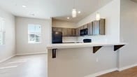 This single-story unit offers a well-organized layout with distinct living, kitchen, bedroom, and bathroom areas finished in a consistent, neutral palette throughout. The kitchen serves as a central feature, equipped with dark espresso-toned cabinetry that extends to the upper and lower sections of the walls, providing generous storage. Black appliances, including a refrigerator, range, and over-the-range microwave, complement the cabinetry. A peninsula with a white countertop and decorative bracket supports doubles as a breakfast bar, separated from the adjacent dining and living areas by a half-wall. Pendant lighting hangs above the peninsula, adding a functional yet stylish accent. Light wood-style flooring runs through the kitchen and living areas, offering easy maintenance and a clean aesthetic. Natural light enters through multiple windows fitted with horizontal blinds. The bedrooms feature plush carpeting, ceiling fans, and reach-in closets with double hanging rods and shelving. The bathrooms are finished with matching dark vanity cabinetry, white countertops, and a tub-shower combination with brushed nickel fixtures, all set on light wood-style flooring for a cohesive look.