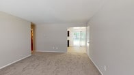 This single-floor residence offers a thoughtfully designed layout with a neutral color palette and consistent finishes throughout. The living area greets residents with plush carpeting, soft taupe walls, and a large window alongside a sliding glass door that fills the space with natural light and provides direct access to an outdoor area with views of surrounding greenery.

The kitchen is a functional highlight, featuring rich dark-wood cabinetry with gold hardware, light-toned countertops, and a full suite of stainless steel appliances including a gas range, built-in microwave, dishwasher, and refrigerator. Light hardwood-style flooring ties the kitchen together cleanly.

Multiple carpeted bedrooms provide comfortable and well-sized living spaces, each with large windows fitted with blinds to control natural light. One bedroom includes a small access panel on the wall, adding a practical element to the design.

The bathroom is cleanly appointed with tile flooring in warm earth tones, a tiled tub-shower surround, a dark-wood vanity with a white countertop, and standard fixtures. A dedicated laundry room with built-in shelving, a full-size washer and dryer, and a water heater rounds out the unit's practical amenities, offering excellent in-unit storage and convenience.