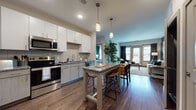This thoughtfully designed single-floor residence offers a contemporary open-concept layout that seamlessly connects the kitchen, dining, and living areas. The kitchen is a standout feature, equipped with stainless steel appliances, white upper cabinetry, two-tone lower cabinets, a subway tile backsplash, granite countertops, and a central island with bar seating illuminated by pendant lighting. Rich hardwood-style flooring flows throughout the main living spaces, complementing the warm, modern aesthetic.

The living area provides a comfortable, relaxed atmosphere with access to natural light through large windows and glass doors. Two generously sized bedrooms feature plush carpeting and large windows that invite abundant natural light. Each bedroom is distinguished by a bold accent wall — one in deep emerald green and the other in a calming teal — adding character and visual interest.

Two full bathrooms serve the residence. One includes a tiled soaking tub and shower combo with a granite vanity, while the en-suite bathroom features a walk-in glass shower, an extended granite vanity, and direct access to a walk-in closet. Throughout, the design balances modern finishes with warm, inviting tones, creating a cohesive and functional living environment.