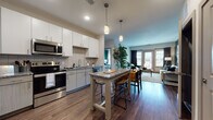 This thoughtfully designed single-floor residence offers a contemporary open-concept layout that seamlessly connects the kitchen, dining, and living areas. The kitchen is a standout feature, equipped with stainless steel appliances, white upper cabinetry, two-tone lower cabinets, a subway tile backsplash, granite countertops, and a central island with bar seating illuminated by pendant lighting. Rich hardwood-style flooring flows throughout the main living spaces, complementing the warm, modern aesthetic.

The living area provides a comfortable, relaxed atmosphere with access to natural light through large windows and glass doors. Two generously sized bedrooms feature plush carpeting and large windows that invite abundant natural light. Each bedroom is distinguished by a bold accent wall — one in deep emerald green and the other in a calming teal — adding character and visual interest.

Two full bathrooms serve the residence. One includes a tiled soaking tub and shower combo with a granite vanity, while the en-suite bathroom features a walk-in glass shower, an extended granite vanity, and direct access to a walk-in closet. Throughout, the design balances modern finishes with warm, inviting tones, creating a cohesive and functional living environment.