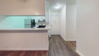 Located at 17808 Sherman Way in Reseda, this single-floor unit offers a well-organized layout with consistent dark hardwood-style flooring throughout, lending a cohesive and polished look to the interior. The living area is generously proportioned, featuring neutral white walls, a textured ceiling, and a wall-mounted HVAC unit. A sliding glass door opens to an outdoor balcony area, allowing natural light to flow in and providing views of surrounding greenery. An open closet nook is conveniently positioned within the living space.

The kitchen is defined by a raised peninsula counter with a light stone-style surface, white cabinetry, and stainless steel appliances including a gas range and refrigerator, along with an overhead range hood. A hallway connects the kitchen to the entry door, maintaining a clear and functional flow.

The bedroom is a quiet, well-lit room with access to a private outdoor space through a sliding glass door and a ceiling fan overhead. The bathroom features a white vanity with an integrated sink, a bathtub with shower, mirrored accents, and a frosted window that provides natural light while maintaining privacy. The overall ambiance is clean, bright, and move-in ready.