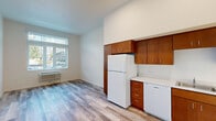 Located at 12495 SW 172nd Terr in Beaverton, Oregon, this one-bedroom, one-bathroom residence offers a well-organized single-floor layout designed for comfortable, efficient living. The interior features light wood-look vinyl plank flooring throughout the main living areas, complemented by clean white walls that create a bright, airy atmosphere.

The kitchen is a functional highlight, featuring warm wood cabinetry that extends to the ceiling for generous storage, white appliances including a refrigerator, dishwasher, and electric range, and a double-basin sink set into light-colored countertops. The elevated ceiling in the kitchen area adds a sense of openness.

The living room benefits from a large window with vertical blinds that allows abundant natural light and outdoor views. An in-wall HVAC unit provides climate control. The space flows naturally from the kitchen into the living area via wood-look flooring.

The spacious bedroom is carpeted in a neutral blue-grey tone and features its own large window for natural light, a dedicated closet, and direct access to the bathroom. The bathroom includes a full tub/shower combination, vanity with mirror, wood-toned cabinetry, and warm hardwood-style flooring, completing this thoughtfully designed residence.