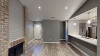 This single-story, 2-bedroom, 2-bathroom home offers a thoughtfully designed layout with modern finishes throughout. Wood-look flooring flows seamlessly across all main living areas, complementing the neutral gray walls and white trim that define the home's clean, contemporary aesthetic.

The living room serves as a focal point, highlighted by a striking full-height brick fireplace and vaulted ceiling that adds a sense of openness and character. A sliding glass door and additional windows allow natural light to fill the space, while recessed lighting provides consistent illumination throughout.

The kitchen opens directly to the living and dining areas via a pass-through counter, creating a connected, functional layout. It features stainless steel appliances, including a gas range, microwave, and refrigerator, paired with gray cabinetry, a subway tile backsplash, and light countertops. Pendant lighting adds a stylish finishing touch.

Both bedrooms are well-proportioned, each equipped with a ceiling fan and wood-look flooring. The two bathrooms are finished with marble-look tile surrounds in the tub/shower combinations, dark gray vanity cabinetry, and framed mirrors, delivering a polished, updated look throughout.