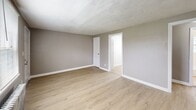 Located at 2300 S Broad St in Trenton, NJ, this 2-bedroom, 1-bathroom unit offers a practical and well-appointed single-floor layout. Light wood laminate flooring runs throughout, lending a clean, cohesive look to every room. The kitchen is efficiently designed with white shaker-style cabinetry, marble-look countertops, white subway tile backsplash, a stainless steel sink, and black appliances including a gas range and refrigerator. Natural light filters in through a window fitted with blinds, and a classic cast-iron radiator provides reliable heating. A connecting hallway links the kitchen to the rest of the unit. Both bedrooms are finished in neutral gray tones with light wood flooring, individual windows for natural light, and cast-iron radiators. The primary bedroom includes a closet, while the second bedroom also features a dedicated closet. The living room is open and airy, with a window overlooking the exterior and a radiator unit. The bathroom is neatly finished with floor-to-ceiling white subway tile in the tub surround, a soaking tub with shower, a gray vanity with a mirror framed in a barn-style accent, and a frosted window for privacy. Overall, the unit presents a clean, updated aesthetic with functional classic details throughout.