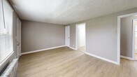 Located at 2300 S Broad St in Trenton, NJ, this 2-bedroom, 1-bathroom unit offers a practical and well-appointed single-floor layout. Light wood laminate flooring runs throughout, lending a clean, cohesive look to every room. The kitchen is efficiently designed with white shaker-style cabinetry, marble-look countertops, white subway tile backsplash, a stainless steel sink, and black appliances including a gas range and refrigerator. Natural light filters in through a window fitted with blinds, and a classic cast-iron radiator provides reliable heating. A connecting hallway links the kitchen to the rest of the unit. Both bedrooms are finished in neutral gray tones with light wood flooring, individual windows for natural light, and cast-iron radiators. The primary bedroom includes a closet, while the second bedroom also features a dedicated closet. The living room is open and airy, with a window overlooking the exterior and a radiator unit. The bathroom is neatly finished with floor-to-ceiling white subway tile in the tub surround, a soaking tub with shower, a gray vanity with a mirror framed in a barn-style accent, and a frosted window for privacy. Overall, the unit presents a clean, updated aesthetic with functional classic details throughout.