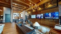 Located at 1425 Semmes Ave in Richmond, Virginia, this single-floor communal space masterfully combines industrial heritage with contemporary design. The interior is defined by soaring ceilings with exposed wooden beams and trusses, warm hardwood flooring, and prominently featured exposed brick walls that lend the space an authentic, character-rich atmosphere.

The main lounge area is generously proportioned, furnished with a mix of tufted leather sofas, barrel chairs, and accent seating arranged around coffee tables, creating multiple intimate conversation zones. A striking candelabra-style chandelier anchors the space overhead, while wall-mounted flat-screen televisions are integrated into a slatted wood feature wall. Large floor-to-ceiling windows flood the interior with natural light and offer views of the surrounding neighborhood.

A dedicated café-style area features marble-topped bistro tables, built-in banquette seating along the windows, pendant lighting, and a sleek service counter equipped with beverage amenities. A welcoming entry zone displays bold, graphic wall lettering and eclectic décor against exposed brick. An additional mailroom area presents a bold monochromatic graphic floor, resident mailboxes, and motivational wall typography, completing this thoughtfully designed, multifunctional community space.