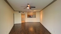 Located in Dallas, TX, this single-floor residence offers a well-designed layout that balances functionality and comfort. The main living area is a standout feature, showcasing rich, dark hardwood-style flooring that extends throughout the open floor plan, creating a warm and cohesive aesthetic. Crown molding lines the ceiling, adding a refined architectural detail that elevates the overall design.

A ceiling fan with a built-in light fixture serves as a central element of the living space, providing both practical airflow and ambient lighting. Track lighting is also present, offering additional illumination and flexibility. The neutral wall tones throughout the space create a versatile backdrop suited to a variety of interior styles.

The kitchen is accessible via a pass-through counter opening directly into the living area, promoting an open and connected feel. Warm wood cabinetry, dark granite or stone countertops, and stainless steel appliances — including a built-in microwave and range — make the kitchen both attractive and functional. A hallway connects the main living areas to additional rooms within the residence, offering a clear and intuitive flow throughout the home. Altogether, this Dallas property presents a clean, move-in-ready space with thoughtful finishes.