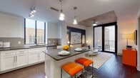This single-floor residence offers two bedrooms and two bathrooms within a thoughtfully designed open-concept layout that blends contemporary urban aesthetics with functional living. The kitchen serves as a central hub, featuring white shaker cabinetry, dark countertops, a tile backsplash, and a full suite of stainless steel appliances including a refrigerator, range, microwave, and dishwasher. A central island with pendant lighting provides casual seating and additional prep space, flowing seamlessly into the living area, which offers access to a private balcony through floor-to-ceiling windows that draw in abundant natural light.

Both bedrooms feature plush carpeting, ceiling fans, and large windows with exterior views. The primary bedroom showcases an exposed concrete ceiling, bold accent wallcovering, and direct access to a full bathroom with white cabinetry, dark countertops, a backlit mirror, and a walk-in closet. The second bedroom mirrors a similar aesthetic with herringbone accent wallcovering. A second full bathroom with matching finishes serves the remaining bedroom. A dedicated laundry closet with a stacked washer and dryer, along with dark hardwood-style flooring throughout the main living areas, completes this well-appointed residence.