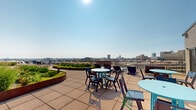 Located at 808 S Wells St in Chicago's South Loop neighborhood, this rooftop terrace offers a distinctive outdoor retreat elevated above the city. The space is defined by generously landscaped garden beds with curved, Corten steel-edged planters filled with a rich variety of flowering plants, ornamental grasses, ground cover, and seasonal greenery — lending the terrace a vibrant, living character throughout the warmer months.

The terrace is thoughtfully arranged with multiple seating zones to accommodate a range of uses. Casual lounge areas feature Adirondack-style chairs and chaise lounges for relaxed sunbathing, while bistro-style tables with chairs offer spaces for dining or small group gatherings. Additional conversation groupings with low lounge chairs and side tables are positioned to take full advantage of the surrounding views.

Broad pavers in a neutral tone span the terrace, providing ample open circulation space between the seating areas and garden installations. A perimeter railing encloses the space safely while preserving unobstructed sightlines in all directions.

The panoramic views are a defining feature — the Chicago skyline rises prominently to the north, while expansive city vistas stretch in every direction under open skies. Natural light floods the terrace throughout the day, creating a bright and energizing atmosphere well-suited for both active use and quiet relaxation.
