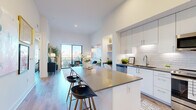 This thoughtfully designed one-bedroom, one-bathroom residence offers a modern open-concept layout that maximizes its well-proportioned footprint. The combined kitchen and living area serves as the heart of the home, featuring soaring ceilings that amplify the sense of space and an abundance of natural light. The kitchen is outfitted with sleek white cabinetry extending to the ceiling, a textured tile backsplash, stainless steel appliances, dark quartz countertops, and a central island with bar seating — ideal for both cooking and casual dining. A built-in nook adjacent to the kitchen provides a convenient workspace. The living room opens directly onto a private balcony through floor-to-ceiling sliding glass doors, offering sweeping city views and seamless indoor-outdoor flow. The bedroom is a comfortable retreat, featuring a large window with city views, a dedicated closet, and warm hardwood-style flooring consistent throughout the unit. The bathroom is a standout feature, appointed with marble-look tile flooring, an extended double vanity with wood-toned cabinetry and backlit mirrors, and a glass-enclosed soaking tub and shower combination. A hallway connects the private areas of the residence, completing this cohesive and stylish urban living space.
