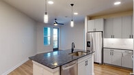 Located at 180 Newton Bridge Rd in Athens, GA, this well-appointed one-bedroom, one-bathroom unit offers a thoughtfully designed layout across a single floor. The open-concept kitchen and living area serves as the heart of the home, anchored by a central island with a deep granite countertop and an undermount sink. White shaker-style cabinetry lines the kitchen walls, complemented by a full suite of stainless steel appliances including a French door refrigerator, electric range, built-in microwave, and dishwasher. Light hardwood-style flooring extends throughout the main living areas, while recessed lighting and stylish pendant fixtures over the island provide ample illumination. A ceiling fan in the living area and natural light from a window with exterior views add to the airy ambiance. The bedroom features plush carpeting, a ceiling fan, and a large window that invites natural light, creating a comfortable retreat. A dedicated walk-in closet with built-in shelving and hanging rods offers generous storage. The bathroom is finished with a dark granite vanity countertop, white shaker cabinetry with matte black hardware, and a tub-shower combination, all set on light hardwood-style flooring for a clean, cohesive look.