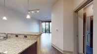 This contemporary 610 square foot apartment in Domain Brewers Hill, Baltimore, offers a thoughtful blend of comfort and style. The open-concept layout maximizes the use of space, seamlessly connecting the living area and kitchen. The kitchen is a standout feature, boasting stainless steel appliances, granite countertops, and rich wood cabinetry with a built-in wine rack. A breakfast bar provides additional seating and workspace.

The living area is bathed in natural light from large windows, which also offer views of the surrounding area. Dark wood flooring in the main living space contrasts beautifully with the neutral walls, creating a warm and inviting atmosphere. The spacious 220 square foot primary bedroom features plush carpeting and ample closet space.

Throughout the apartment, you'll find modern amenities such as recessed lighting, ceiling fans, and stylish fixtures. The bathroom, while not pictured, likely continues the contemporary aesthetic of the rest of the space. With its thoughtful design and prime location in Baltimore's Brewers Hill neighborhood, this apartment offers an ideal urban living experience.