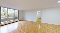 Located at 100 Eighth Ave in Kitchener, Ontario, this 2-bedroom, 1-bathroom unit offers a well-organized layout across a single floor. Warm parquet hardwood flooring flows consistently throughout the living areas and bedrooms, lending a classic, cohesive character to the space.

The spacious living room is a standout feature, anchored by large floor-to-ceiling windows that invite natural light and open onto a private balcony. From the balcony, views of mature trees and landscaped green space provide a tranquil outdoor outlook. The open, clean-lined living area connects seamlessly to the hallway, which leads to the rest of the unit.

The kitchen features light-toned tile flooring, white cabinetry, and a stainless steel electric range, offering a functional and tidy cooking space. The full bathroom is finished with white tile surrounding the tub-shower combination, light tile flooring, and a vanity with a stone-look countertop, complemented by a grab bar for added accessibility.

The primary bedroom is generously sized, featuring a window with views of the surrounding neighbourhood and a dedicated walk-in closet with dual hanging rods and built-in shelving. The second bedroom also features parquet flooring and a bright window. A welcoming entry hallway with a closet completes the practical layout of this well-maintained unit.