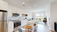 Located at 1215 N Fayette St in Alexandria, VA, this well-appointed one-bedroom, one-bathroom residence offers a thoughtfully designed open-concept layout. The combined kitchen and living area serves as the heart of the home, featuring light hardwood flooring, recessed lighting, and a large picture window that floods the space with natural light and frames views of the surrounding cityscape.

The kitchen is outfitted with white cabinetry, a white subway tile backsplash, warm wood open shelving, and a full suite of stainless steel appliances including a refrigerator, electric range, built-in microwave, and dishwasher. A white kitchen island with bar seating provides additional prep space and a casual dining option. The living area flows seamlessly from the kitchen, creating an airy and functional gathering space.

The bedroom is a comfortable retreat, featuring a large window with city views, neutral tones, and direct access to multiple closets—five in total throughout the unit, offering exceptional storage. The bathroom includes a tub and shower combination enclosed by a frameless glass door, with large-format neutral tile surround and clean, modern fixtures. The overall aesthetic is contemporary and cohesive, with a bright, clean palette throughout.
