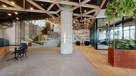 Located at 49 Fisk St in Jersey City, NJ, this striking 3,860-square-foot single-floor commercial lobby space exemplifies contemporary biophilic design. The most immediately commanding architectural feature is the geometric wood-lattice ceiling, a bold interlocking triangular framework finished in warm natural wood tones set against a dark ceiling plane, lending a sense of grandeur and visual depth throughout the entire space.

The floor transitions between warm wide-plank hardwood and neutral stone-toned tile, delineating distinct functional zones. A sculptural concrete staircase anchored by exposed cylindrical concrete columns serves as a dramatic central element, flanked by lush tiered planters with verdant greenery that cascade down its sides. Corten steel planter boxes add a rich, industrial warmth throughout.

A reception desk offers a welcoming entry point, while a café station with bar-height seating provides a casual gathering area. A lounge zone features deep green velvet armchairs arranged around a mosaic-topped table, set against a geometric triangular shelving wall that mirrors the ceiling design. Additional seating nooks with teal upholstered benches and private phone booths provide flexible work options. Floor-to-ceiling black-framed glass partitions and large street-facing windows flood the space with natural light.