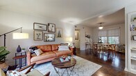 This single-floor residence showcases a thoughtfully curated mid-century modern aesthetic carried throughout its well-defined living spaces. The living room serves as the heart of the home, featuring rich dark hardwood floors, crown molding, and an abundance of natural light streaming through large windows fitted with roller shades. A tufted cognac leather sofa anchors the space, complemented by a geometric area rug, a round wood-and-metal coffee table, and an eclectic gallery wall of framed artwork that adds character and warmth.

The separate dining area continues the hardwood flooring and opens to natural greenery views through its window, centered around a round dining table with mid-century wishbone chairs beneath a globe pendant light. Adjacent, the kitchen features a retro-inspired design with two-tone cabinetry — sage lower cabinets paired with light upper cabinets — over a bold black-and-white checkered tile floor, a gas range, and a window that brings in natural light.

The bedroom is a serene retreat with hardwood floors, diffused natural light through sheer roller shades, and a statement wood headboard with a chevron inlay pattern. The bathroom retains its vintage charm with floor-to-ceiling peach ceramic tile surround and a soaking bathtub, offering a distinctly retro character that ties the home's personality together cohesively.