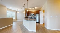 Located at 4135 Kenvil Dr in North Port, Florida, this single-floor residence presents a thoughtfully designed layout with a cohesive blend of practical and modern finishes. The entryway welcomes residents through a paneled front door topped with a transom window, allowing natural light to filter into the foyer, which features light wood-look flooring that extends into the main living areas.

The open-concept kitchen and living space serves as the heart of the home. The kitchen is equipped with stainless steel appliances, including a refrigerator, range, and over-the-range microwave. Rich wood-toned cabinetry reaches toward the ceiling, complemented by granite countertops. A curved kitchen island with a built-in sink adds additional workspace and seating potential. Pendant lighting illuminates the island, while a separate laundry area is conveniently tucked nearby.

The living and dining areas are generously proportioned, with large windows providing ample natural light and views of the surrounding landscape. Bedrooms feature plush carpeting, ceiling fans, and windows with blinds. The bathrooms are finished with granite-topped vanities, wood-toned cabinetry, and light wood-look tile flooring. A staircase with carpet treads and a pendant light fixture connects to additional levels of the home.