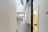 Located at 220 Herald Pl in Syracuse, NY, this 2-bedroom, 2-bathroom loft-style residence offers a distinctive industrial-chic aesthetic defined by dramatically high ceilings, exposed metal ductwork, and dark hardwood flooring that runs throughout the main living areas. The open-concept layout seamlessly connects the living room and kitchen, creating a generous, airy atmosphere. The living room features a built-in fireplace and is bathed in natural light from large industrial-style windows, enhancing the spacious feel. The kitchen is well-appointed with white shaker cabinetry, granite countertops, stainless steel appliances including a dishwasher, and pendant lighting that complements the loft character. Both bedrooms are carpeted and offer tall ceilings, with one featuring a large window overlooking the surrounding area and exposed ductwork overhead. Three closets provide ample storage throughout the unit. The two bathrooms are finished with tile flooring, white vanities, granite countertops, and round mirrors, lending a clean and classic look. A utility room rounds out the floor plan. The combination of industrial architectural details and modern finishes gives this space a unique urban character ideal for city living.