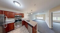 Located at 277 E Allen St, Unit 313 in Winooski, Vermont, this one-bedroom, one-bathroom unit offers a thoughtfully designed single-level layout. The open-concept kitchen and living area serves as the heart of the home, where rich cherry-toned cabinetry, stainless steel appliances — including a refrigerator, range, microwave, and dishwasher — and granite-style countertops create a functional and attractive cooking space. A peninsula with a double-basin sink and pendant lighting overhead adds both workspace and visual separation from the carpeted living area, which benefits from natural light through a large window. A wall-mounted mini-split unit provides efficient climate control. The spacious bedroom features plush carpeting, multiple windows with roller shades that frame views of surrounding greenery, and a closet for storage. Additional storage is provided by a dedicated pantry. The bathroom is finished with tile flooring and includes a full soaking tub with shower. Neutral warm tones throughout, clean white trim, and consistent flooring choices give the unit a cohesive and move-in-ready feel.