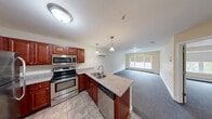 Located at 277 E Allen St, Unit 313 in Winooski, Vermont, this one-bedroom, one-bathroom unit offers a thoughtfully designed single-level layout. The open-concept kitchen and living area serves as the heart of the home, where rich cherry-toned cabinetry, stainless steel appliances — including a refrigerator, range, microwave, and dishwasher — and granite-style countertops create a functional and attractive cooking space. A peninsula with a double-basin sink and pendant lighting overhead adds both workspace and visual separation from the carpeted living area, which benefits from natural light through a large window. A wall-mounted mini-split unit provides efficient climate control. The spacious bedroom features plush carpeting, multiple windows with roller shades that frame views of surrounding greenery, and a closet for storage. Additional storage is provided by a dedicated pantry. The bathroom is finished with tile flooring and includes a full soaking tub with shower. Neutral warm tones throughout, clean white trim, and consistent flooring choices give the unit a cohesive and move-in-ready feel.