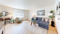 Located at 6100 Edinger Ave in Huntington Beach, California, this single-floor 2-bedroom, 2-bathroom unit offers a well-organized layout across a comfortable footprint. Light wood flooring runs through the main living areas, lending a bright, airy feel that is complemented by crisp white walls throughout.

The living room is generously proportioned, featuring a large window with vertical blinds that floods the space with natural light. Built-in shelving along one wall provides ample display and storage space. The living area flows seamlessly into the dining room, which benefits from its own window and a ceiling fan, creating an inviting space for meals.

The galley-style kitchen is efficiently designed with white cabinetry lining both sides, light countertops, and wood-toned flooring, providing functional workspace and storage.

Both bedrooms are carpeted and well-lit, with large windows dressed in vertical blinds. The spacious primary bedroom comfortably accommodates a king-sized bed and additional furniture. Each bedroom is served by its own bathroom, with at least one bathroom featuring a full shower-tub combination.

A connecting hallway ties the rooms together, completing a practical and cohesive floor plan well-suited for comfortable living in the heart of Huntington Beach.